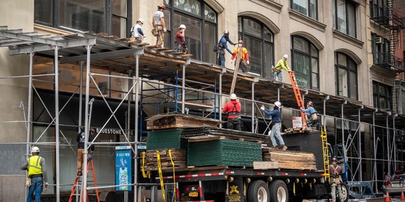 Construction workers unload material from a truck to other workers standing on scaffolding