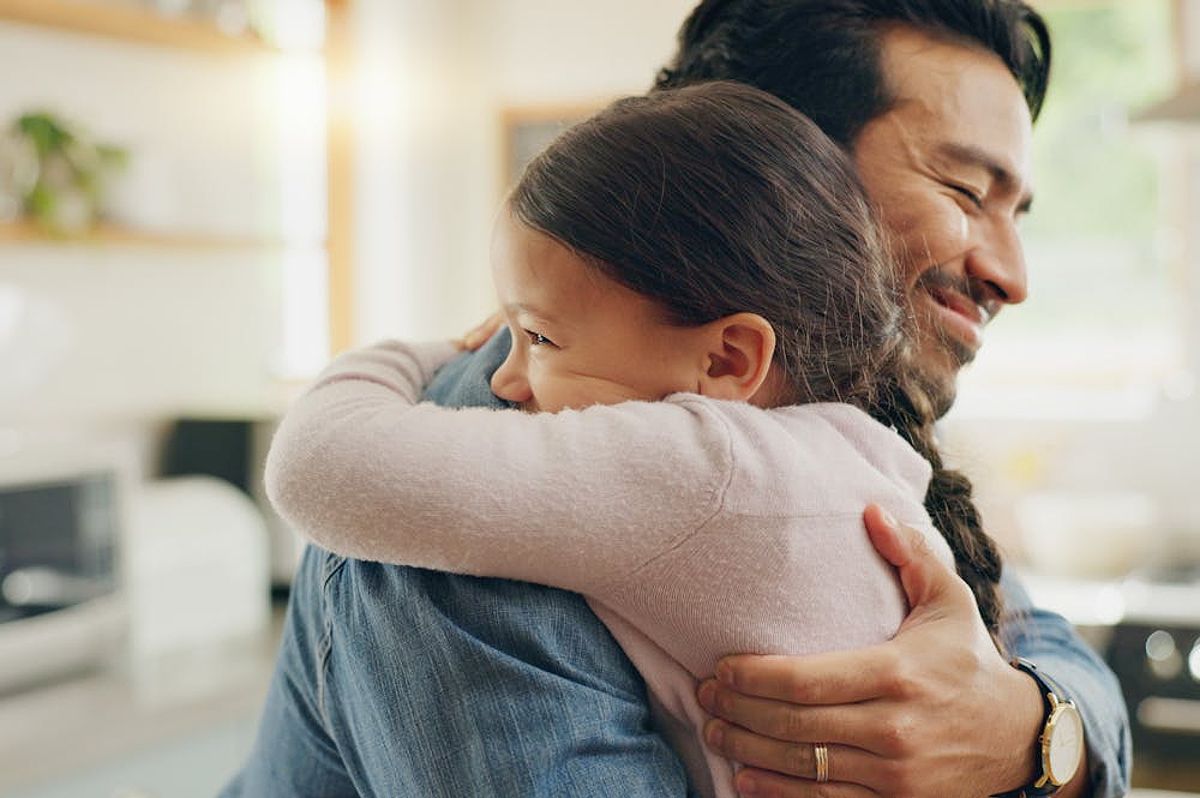 A young girl hugs a smiling man, likely her father, in a warmly lit home setting.