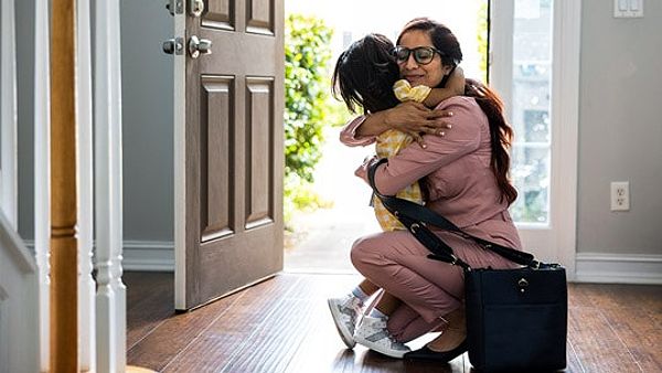 Woman crouching to hug child in front of an open door